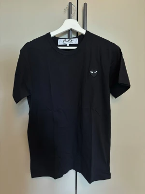 Svart Comme des Garçons PLAY t-shirt - Svart t-shirt från Comme des Garçons PLAY med det ikoniska hjärtemblemet med ögon på bröstet. Klassisk rund halsringning och korta ärmar. Tillverkad i 100% bomull för en skön och avslappnad känsla..                                Använd någon gång endast! Har ej kvitto!  