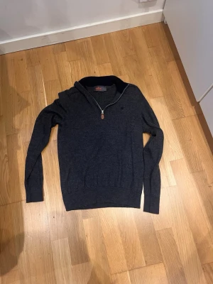 Mörkblå stickad tröja från Morris - Snygg mörkblå stickad tröja från Morris i 100% merinoull. Tröjan har halv dragkedja, hög krage och diskret logga på bröstet. Perfekt för dig som gillar klassisk och stilren design.