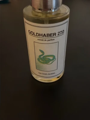 Goldhaber 27.0 (God of fire) - Unik parfymflaska med etikett där det står Goldhaber 27.0. Flaskan är cylindrisk i genomskinligt glas med silverfärgad kork.  Märket är one bold chemist. Ca 49/50 ml kvar. Pris är diskuterbart!