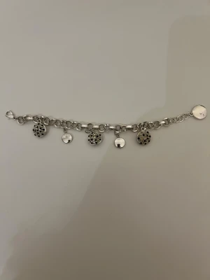 Silverfärgat armband med berlocker - Snyggt armband i silverfärg med grova länkar och flera runda berlocker. Vissa berlocker har små svarta stenar som ger en cool kontrast, medan andra är släta och blanka. Perfekt accessoar för att lyfta din outfit med lite extra bling.