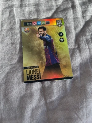 FIFA 365 samlarkort Lionel Messi - Unikt samlarkort från FIFA 365-serien med Lionel Messi i Barcelona-tröja. Kortet har guldglänsande bakgrund och färgstarka detaljer, samt texten 'Top Master' och spelarstatistik. Perfekt för samlare av fotbollskort.
