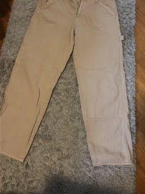 Beige jeans med raka ben - Säljer ett par beige jeans med flera praktiska fickor. Byxorna har klassisk work wearmodell med fickor på sidorna och bak. Perfekta för en avslappnad och trendig stil. Materialet känns mjukt och slitstarkt.