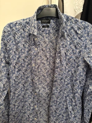Blommig skjorta från Bruun & Stengade - Snygg skjorta från Bruun & Stengade i modern fit med blått och vitt blommönster. Skjortan har klassisk krage, långa ärmar och knäppning framtill. Tillverkad i lättskött material för enkel vardag.
