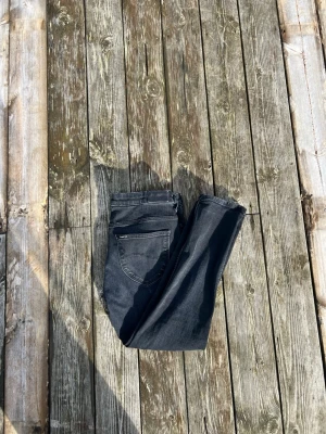 Svarta jeans från Lee - Snygga svarta jeans från Lee med klassisk femficksdesign och raka ben. Jeansen har en diskret Lee-logga på bakfickan och är tillverkade i ett mjukt denimtyg som ger en bekväm känsla. Perfekta för en avslappnad och stilren look.
