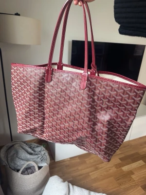 Vinröd shoppingväska - Snygg vinröd shoppingväska med klassiskt mönster i vitt och vinrött. Väskan har dubbla långa handtag och är perfekt för dig som vill ha en rymlig och trendig väska till vardagen. Ej aut3ntisk.