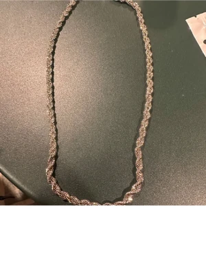 Silvrigt tvinnat pärlhalsband - Snyggt halsband med tvinnad design i silverfärg. Halsbandet är dekorerat med små pärlor som ger ett elegant och glittrande intryck. Perfekt accessoar för att lyfta din outfit med lite extra bling.