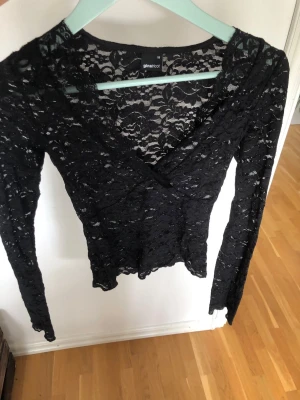 Svart spetsblus från Gina Tricot - Säljer en svart långärmad spetsblus från Gina Tricot. Blusen har v-ringning och är helt i genombruten spets med blommigt mönster. Perfekt för dig som vill ha en snygg och trendig topp med lite edge.