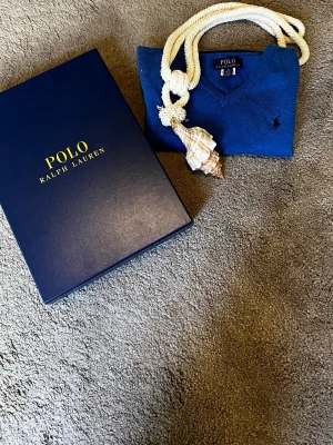 Blå stickad tröja från Polo Ralph Lauren - Snygg blå stickad tröja från Polo Ralph Lauren med V-ringning och klassisk broderad logga på bröstet. Tröjan har långa ärmar och ribbade muddar vid ärmslut och nederkant. Perfekt för lager på lager och stilrena outfits.