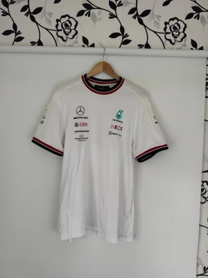 Vit Mercedes AMG Petronas t-shirt XL - Vit t-shirt från Mercedes AMG Petronas Formula One Team med tryckta loggor på bröstet och ärmarna. Använd några gånger. Nypris ca 700:-