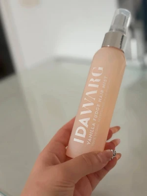 IDAWARG Vanilla Fudge Hair Mist - Fräsch face mist från IDAWARG med doft av vanilj och fudge. Flaskan är ljusbeige med vit text och har en silvrig spraypump. Perfekt för att återfukta och fräscha upp huden under dagen. 100% vegansk formula.