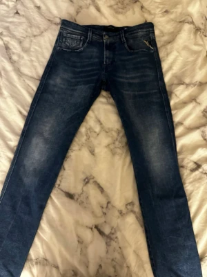 Mörkblå Replay Anbass slim fit jeans - Snygga mörkblå jeans från Replay, modell Anbass med slim fit passform. Jeansen har klassisk femficksdesign, slitningar och tvättade detaljer för en trendig look. Perfekta för dig som gillar en smalare siluett och vill ha ett par stilrena jeans.