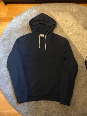 Mörkblå hoodie från Pier One - Snygg mörkblå hoodie från Pier One med klassisk huva och vita dragsnören. Hoodien har en stor magficka och ribbade muddar vid ärmar och nederkant. Perfekt för en avslappnad och stilren look.