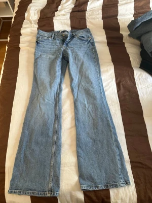 Ljusblå bootcut jeans - Säljer ett par ljusblå bootcut jeans med klassisk femficksdesign och normal midja. Jeansen har utsvängda ben och är tillverkade i denim, vilket ger en tidlös och avslappnad look. Perfekta för dig som gillar retrostil och vill ha ett par snygga jeans i garderoben.