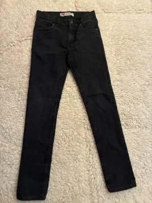 Svarta Levis jeans i modell ”skinny” - Säljer ett par svarta skinny jeans med hög midja och klassisk femficksdesign. Jeansen har smal passform och är tillverkade i stretchigt material för extra komfort. Perfekta till en avslappnad look och lätta att matcha med olika stilar.