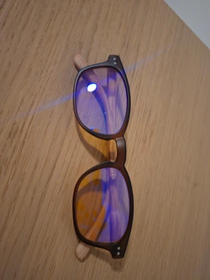 Svarta solglasögon med blåtonade glas (blue light blockers) - Snygga solglasögon med svart, matt båge och blåtonade glas. Bågarna har en klassisk, rundad form och detaljer i trälook på skalmarna. Perfekta för att höja din stil i sommar och skydda ögonen mot solen.