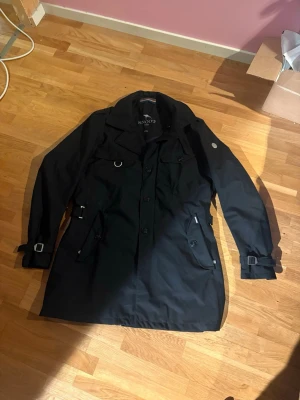 Svart trenchcoat från Snoot  - Stilren svart trenchcoat från Snoot i storlek XXL. Nästintill perfekt skick och riktigt bra kvalité! Passar perfekt över kavajen en blåsig höst eller vinterdag! Skriv vid frågor eller funderingar, priset är förhandlingsbart!!🍁❄️🧣