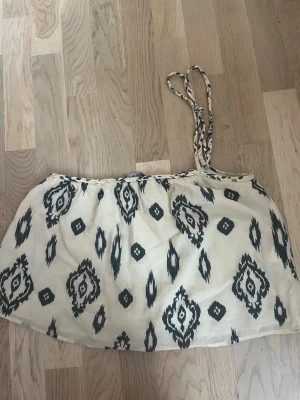 Mönstrad linnetopp från Zara - Säljer en snygg linnetopp från Zara i beige med svart mönster. Toppen har tunna, flätade axelband och ett avslappnat fall. Perfekt för varma dagar och enkel att styla med jeans eller kjol.