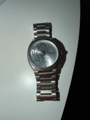 Silverfärgad HEAD vattentät armbandsklocka  - Stilren armbandsklocka i silver med metallänk och rund urtavla. Urtavlan har ett unikt mönster med arabiska siffror och HEAD-loggan. Perfekt accessoar för dig som gillar minimalistisk och modern design.