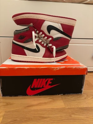 Nike Air Jordan 1 chicago lost and found - Säljer ett par Nike Air Jordan 1 Retro High sneakers i rött, vitt och svart. Skorna har klassisk hög siluett, vit tåbox med perforeringar, svarta swoosh-loggor och röda paneler i läder. Vita skosnören och svart vinge-logo på sidan. Perfekta för dig som gillar streetwear.