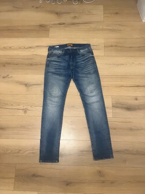 Jack&jones  - Snygga blå slim fit jeans med tydliga slitningar och tvättade detaljer på låren och knäna. Klassisk femficksmodell med normal midja och smala ben. Perfekta för en avslappnad och trendig stil.
