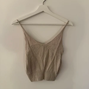 Beige stickad linnetopp - Snygg beige stickad linnetopp med smala axelband och djup v-ringning. Perfekt för varma dagar och enkel att matcha med jeans eller kjol. Toppen har en ribbad nederkant som ger en schysst passform.