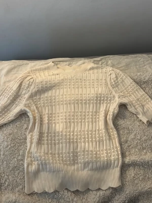 Vit  tröja från Kappahl - Säljer en krämvit stickad tröja från Kappahl i storlek S. Tröjan har ett ribbat mönster med inslag av spetsstickade detaljer, rund halsringning och långa ärmar. Perfekt för dig som gillar en stilren och söt look.