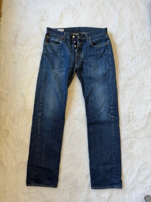 Mörkblå raka jeans - Säljer ett par klassiska mörkblå jeans med rak passform och knappgylf. Jeansen har fem fickor och är tillverkade i ett slitstarkt denimtyg. Perfekta för dig som gillar en tidlös och enkel stil.