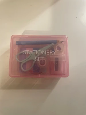 Stationery set i rosa låda - Säljer ett mini stationery set som är oanvänt i en genomskinlig rosa plastlåda. Innehåller sax i mintgrönt, blå penna, pennvässare, tejphållare, tejprulle, suddgummi med björnmotiv och färgglada klisterlappar. Perfekt för skrivbordet eller skolväskan.