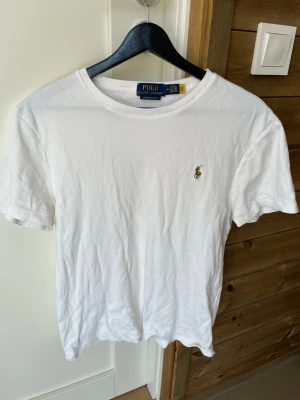 Vit t-shirt från Polo Ralph Lauren - Klassisk vit t-shirt från Polo Ralph Lauren med broderad logga på bröstet. Modellen är slim fit och har rund halsringning samt korta ärmar. Tillverkad i mjuk bomull som känns skön mot huden. Perfekt basplagg för en clean och stilren look.