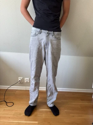 Ljusgrå raka jeans herr - Säljer ett par ljusgrå jeans med rak passform och klassisk femficksdesign. Jeansen har normal midja och är tillverkade i ett mjukt denimtyg. Perfekta för en avslappnad och stilren look. Killen är 188 cm 