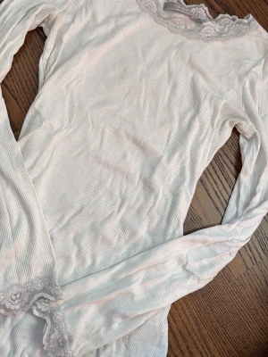 Vit ribbad topp med spets från Fransa - Supersöt vit ribbad topp från Fransa med lång ärm och fina spetsdetaljer vid halsringning och ärmslut. Perfekt att styla med jeans eller kjol för en fräsch look. Jätte snygg till hösten!