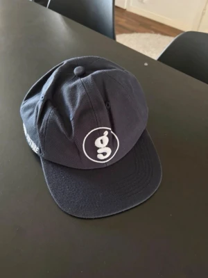 Mörkblå Supreme keps med brodyr - Snygg mörkblå keps från Supreme med vit broderad logga framtill och texten 'SUPREMENOW' samt '4THE FUTURE' på sidorna. Justerbar passform med klassisk röd Supreme-tag baktill. Tillverkad i bomullstyg och har böjd skärm. DEN ÄR LITE DEFORMED!! 
