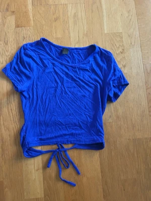 Blå croppad topp med knyt - Lappen är sliten men ser ut som den är ifrån shein. Snygg blå croppad topp med korta ärmar och knyt i ryggen där nere. Perfekt till jeans eller kjol för en trendig look. Tunn och mjuk i materialet, enkel att styla till olika outfits.