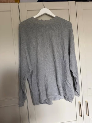 Grå stickad tröja med dragkedja - En stilren grå stickad tröja med lång ärm och rund halsringning. Tröjan har en diskret dragkedja i nacken som ger en snygg detalj. Perfekt för lager-på-lager och enkel att matcha med andra plagg.