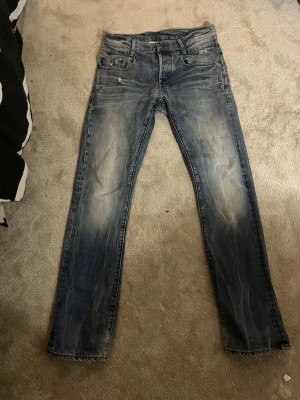 Blå slitna raka G-star jeans slim/bootcut  - Säljer ett par blå jeans med slitningar och tvättade detaljer. Jeansen har raka ben, klassisk femficksmodell och normal midja. Materialet är denim och färgen är en tvättad blå nyans med ljusare partier. Perfekta för en avslappnad och trendig look.