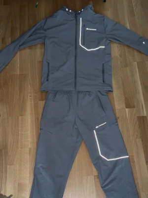 Grå Monterrain Tracksuit - Kostade egentligen 1800kr. Säljer detta gråa träningsset med jacka och byxor. Setet har snygga reflexdetaljer på bröstet och benet, dragkedjor på jackan och fickor på både jacka och byxor. Perfekt för löpning eller utomhusträning när det är mörkt.