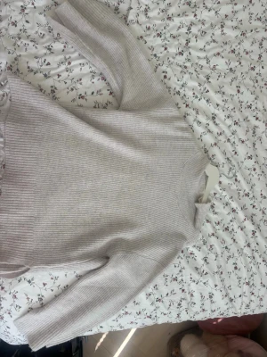 Ljusgrå ribbstickad tröja - Mysig ljusgrå stickad tröja med ribbad struktur och rund hals. Tröjan har långa ärmar och en avslappnad passform, perfekt för lager på lager. Materialet ser ut att vara mjukt och bekvämt, troligen bomull eller ullblandning.