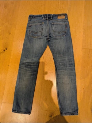 Blåa replay jeans  - Säljer ett par blå replay jeans med raka ben och tydliga slitningar på låret. Jeansen har klassisk femficksdesign och en ljus tvätt med snygga slitdetaljer. Perfekta för en avslappnad och trendig look. pris ej hugget i sten. 