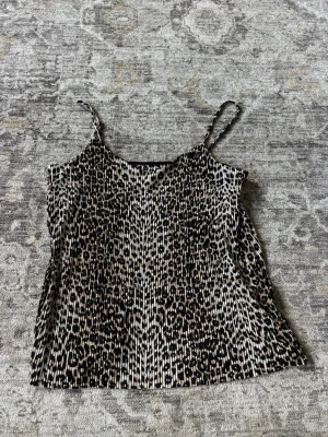 Leopardmönstrad linnetopp - Säljer en leopardmönstrad linnetopp med tunna axelband. Toppen har ett plisserat tyg och är perfekt för dig som vill sticka ut lite extra. Passar till både jeans och kjol för en trendig look.