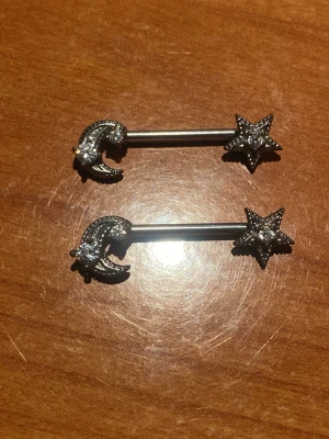 Piercing med måne och stjärna - Nipplepiercing med måne och stjärnor. Längd är 15mm och tjocklek är 1,6 mm. Säljes för 30kr