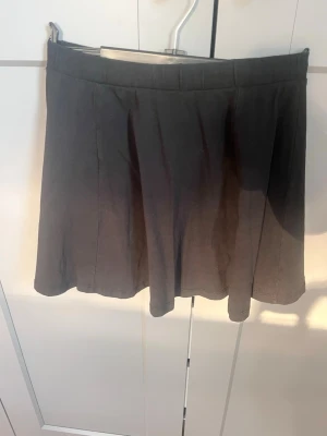 Svart kortkjol med enkel design - En svart kortkjol med enkel och stilren design. Kjolen har en lätt utställd form och bred linning. Perfekt att matcha med olika toppar för en clean look. Tillverkad i ett mjukt material som känns bekvämt hela dagen.