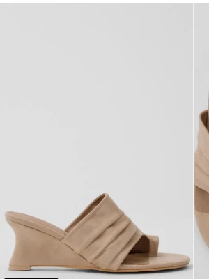 Beige kilklackade sandaler - Snygga beige sandaler med kilklack och breda, vadderade band över foten. Tillverkade i ett mjukt material som ser ut som mocka. Öppen tå och slip-in modell ger en avslappnad men trendig look.