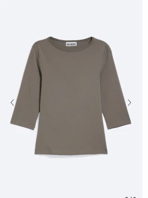 Olivgrön trekvartsärmad topp  - En stilren olivgrön topp från Weekday med trekvartsärm och rund halsringning. Tillverkad i mjuk bomull för en bekväm känsla. Perfekt att matcha med jeans eller kjol för en enkel och clean look.