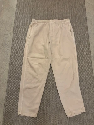 Beige mjukisbyxor från ZARA - Säljer ett par beige mjukisbyxor från ZARA med avslappnad passform och resår i midjan. Byxorna har sidofickor och är tillverkade i ett mjukt material som känns skönt mot huden. Perfekta för chill dagar eller när du vill ha det bekvämt.
