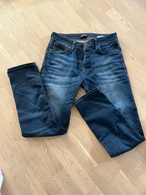 Jeans Jack & jones - Säljer ett par mörkblå jeans med raka ben och snygga kontrastsömmar. Jeansen har klassiska fem fickor och subtila slitningar framtill de har en defekt på baksidan av jeansen därför säljer jag de FÖR 190KR