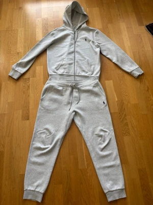 Polo Ralph Lauren tracksuit / mjukisset - Säljer ett komplett grått mjukisset/tracksuit från Polo Ralph Lauren bestående av zip-hoodie och matchande joggingbyxor.  Båda delarna är storlek M och har den klassiska broderade Polo-loggan i mörkblått/svart.  Setet är i fint begagnat skick utan några större anmärkningar. Se bilder för skick. Kvitto finns. 