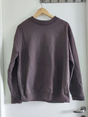 Brun oversized sweatshirt - En enkel och stilren brun sweatshirt med rund hals och ribbade muddar. Oversized passform som ger en avslappnad vibe. Perfekt att matcha med jeans eller mjukisbyxor för en chill look.