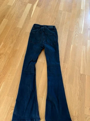 Svarta utsvängda jeans - Säljer ett par svarta jeans med utsvängda ben och klassiska fem fickor. Jeansen har hög midja och är tillverkade i ett mjukt denimtyg som sitter snyggt. Perfekta för dig som gillar retrostil och vill ha ett par riktigt schyssta jeans.