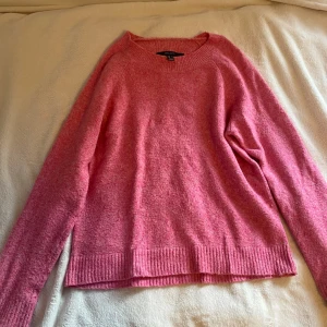 Rosa stickad tröja från Vero Moda - Mysig rosa stickad tröja från Vero Moda med rund halsringning och ribbade muddar vid ärmslut och nederkant. Perfekt för lager på lager och enkel att matcha till olika outfits. Materialet känns mjukt och bekvämt.