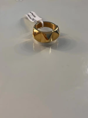 Guldring från Edblad - Snygg guldfärgad ring från Edblad med bred, geometrisk design och blank finish. Ringen har en modern och stilren look som sticker ut och passar perfekt för dig som gillar trendiga accessoarer. Kommer i original ask. Strlk S, 16,8 mm